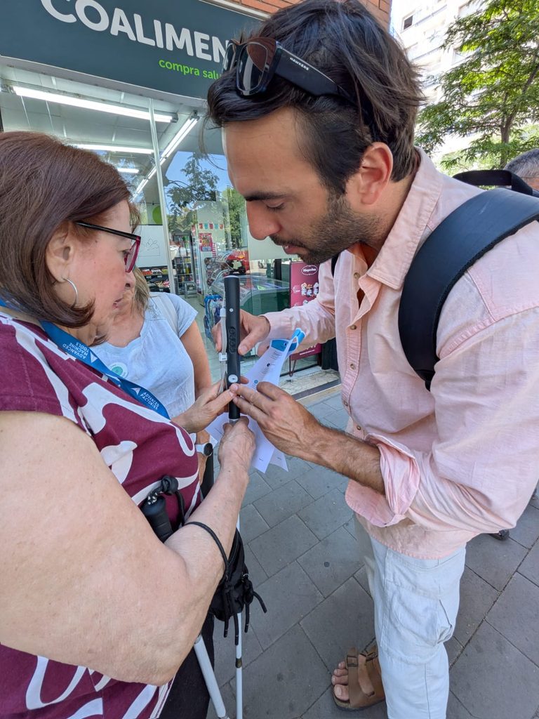 Un home i una dona examinant de prop el mànec del bastó intel·ligent WeWALK 2 al carrer.